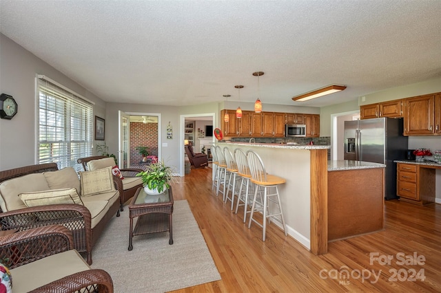 kitchen with a textured ceiling, decorative light fixtures, appliances with stainless steel finishes, and light hardwood / wood-style flooring