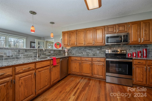 kitchen with stainless steel appliances, tasteful backsplash, light stone countertops, hanging light fixtures, and hardwood / wood-style floors