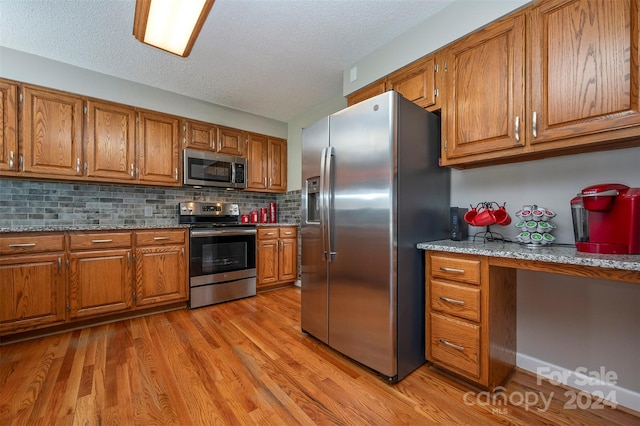 kitchen with stainless steel appliances, light hardwood / wood-style floors, a textured ceiling, backsplash, and light stone countertops