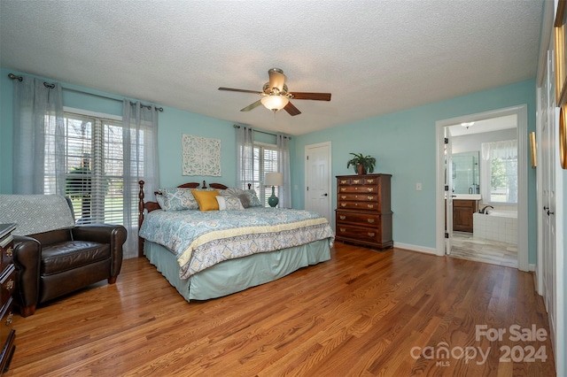 bedroom with multiple windows, hardwood / wood-style flooring, ceiling fan, and ensuite bath