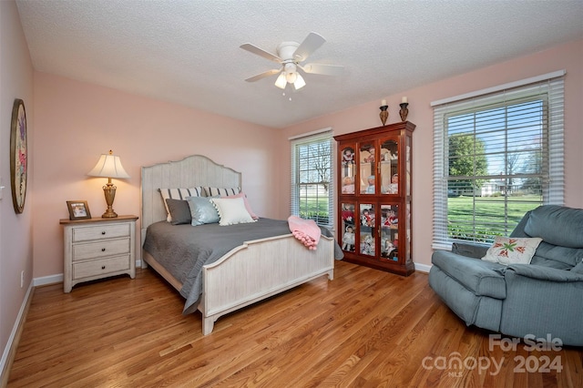 bedroom featuring a textured ceiling, multiple windows, light hardwood / wood-style floors, and ceiling fan