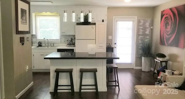 kitchen with pendant lighting, sink, white fridge, white cabinetry, and a breakfast bar area