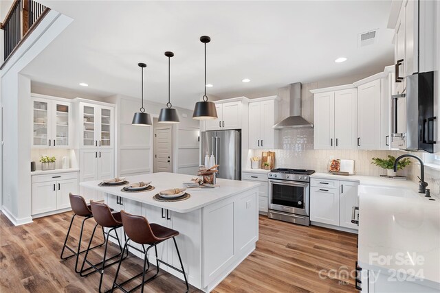 kitchen featuring white cabinets, stainless steel appliances, wall chimney range hood, and a kitchen island