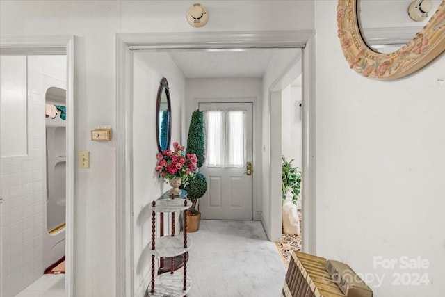 doorway to outside with a textured ceiling and light carpet