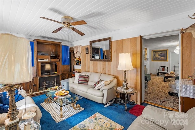 living room featuring ceiling fan, wooden walls, and carpet