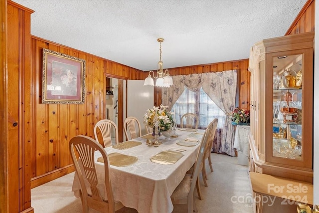 dining space featuring light carpet, a notable chandelier, wood walls, and a textured ceiling