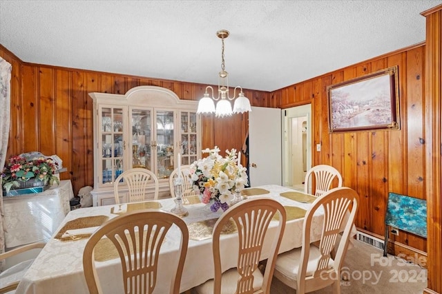 dining room with a notable chandelier, wooden walls, carpet flooring, and a textured ceiling