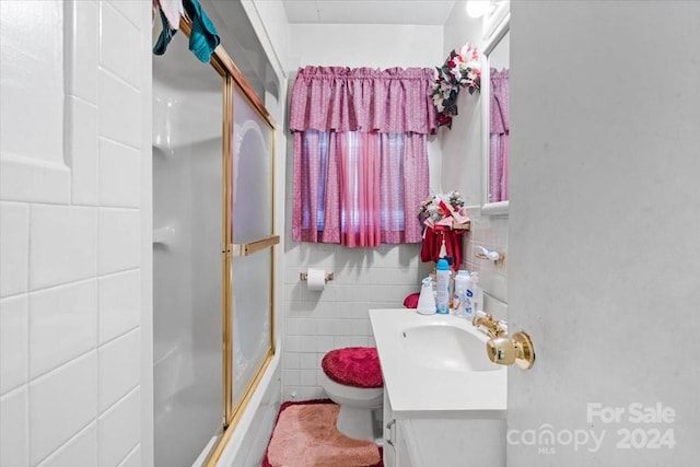 full bathroom featuring bath / shower combo with glass door, vanity, tile walls, and toilet