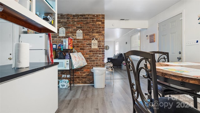 dining space with brick wall and wood-type flooring