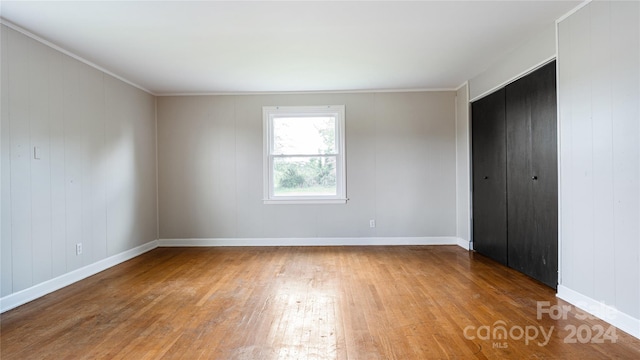 unfurnished bedroom with crown molding, wood-type flooring, and wooden walls