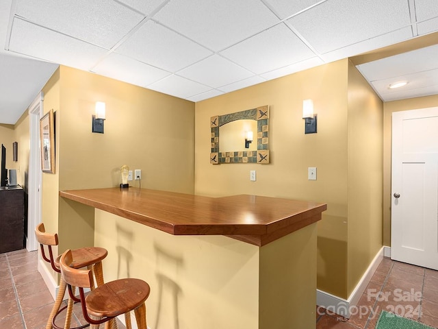 bar featuring a paneled ceiling and dark tile patterned flooring