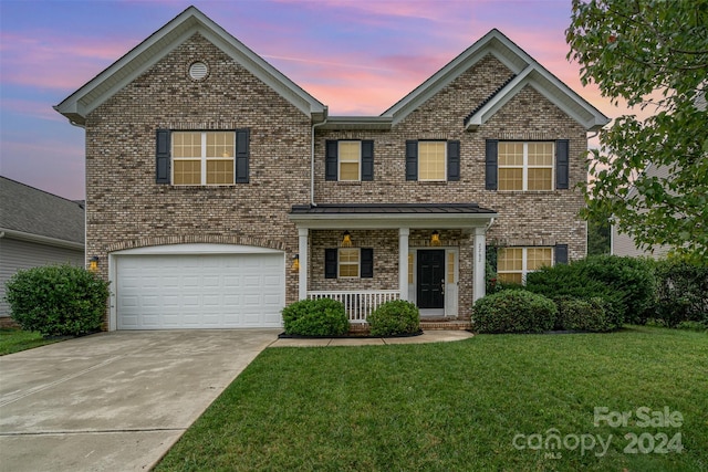 front of property featuring a lawn, covered porch, and a garage