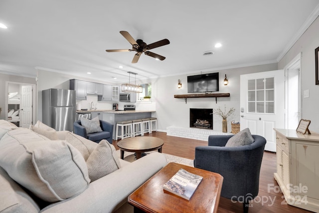 living room with dark wood-type flooring, a fireplace, crown molding, ceiling fan, and sink