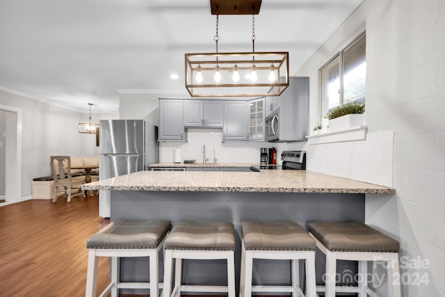 kitchen with decorative light fixtures, gray cabinets, stainless steel appliances, crown molding, and dark hardwood / wood-style flooring