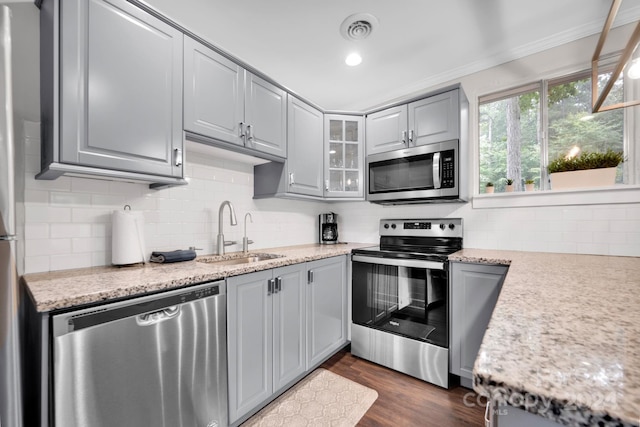 kitchen with light stone counters, sink, dark wood-type flooring, gray cabinets, and appliances with stainless steel finishes