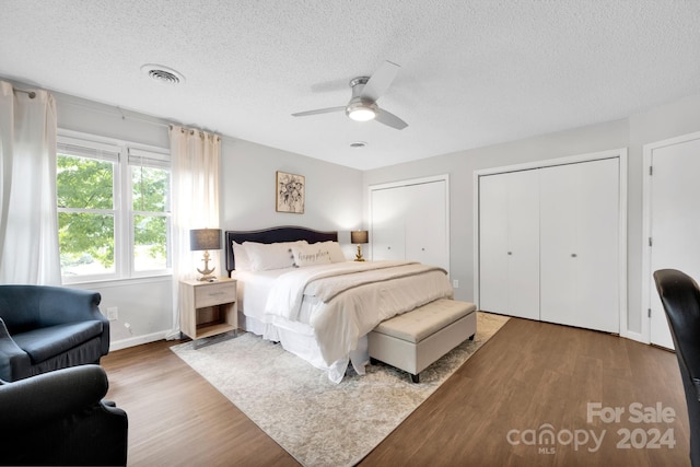 bedroom featuring wood-type flooring, multiple closets, ceiling fan, and a textured ceiling