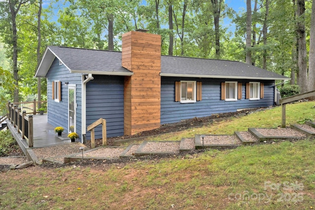 view of property exterior featuring a wooden deck, a lawn, roof with shingles, and a chimney