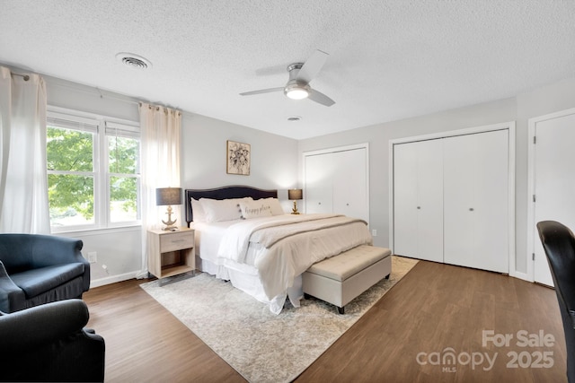 bedroom with visible vents, a textured ceiling, two closets, and wood finished floors