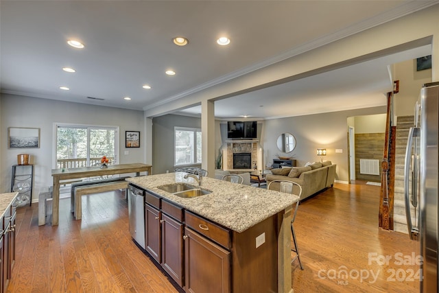 kitchen with a kitchen island with sink, crown molding, light hardwood / wood-style flooring, stainless steel appliances, and a fireplace