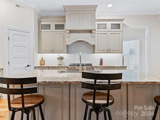 kitchen with light stone counters, crown molding, an island with sink, and light hardwood / wood-style floors