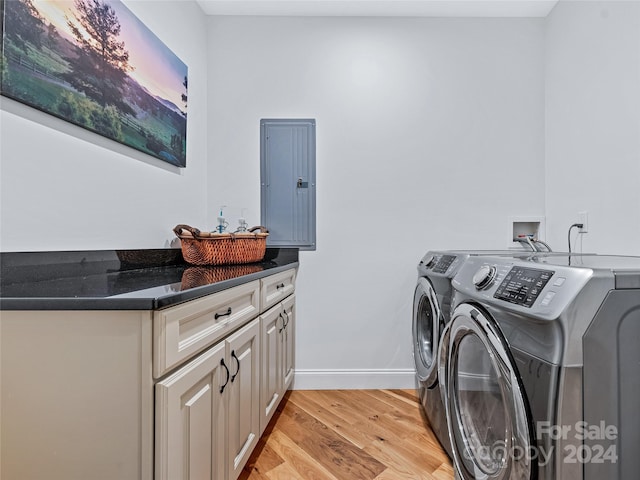 laundry room with electric panel, light hardwood / wood-style flooring, washer and clothes dryer, and cabinets