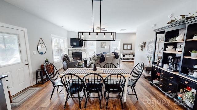 dining room with visible vents, a stone fireplace, and wood finished floors