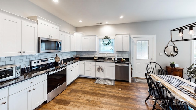 kitchen with tasteful backsplash, white cabinetry, dark wood-style flooring, a sink, and stainless steel appliances