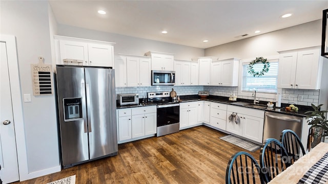 kitchen with tasteful backsplash, appliances with stainless steel finishes, dark countertops, dark wood finished floors, and a sink