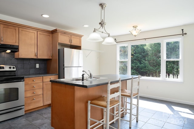 kitchen featuring appliances with stainless steel finishes, backsplash, dark tile patterned floors, hanging light fixtures, and a kitchen island with sink