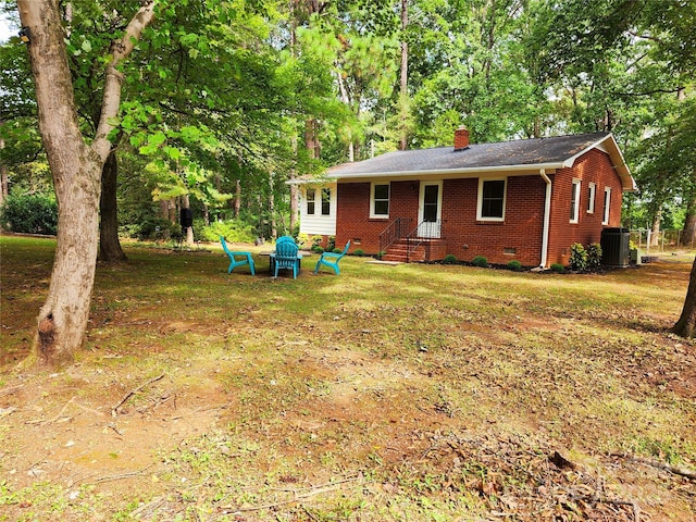 back of property with central air condition unit, brick siding, a yard, crawl space, and a chimney