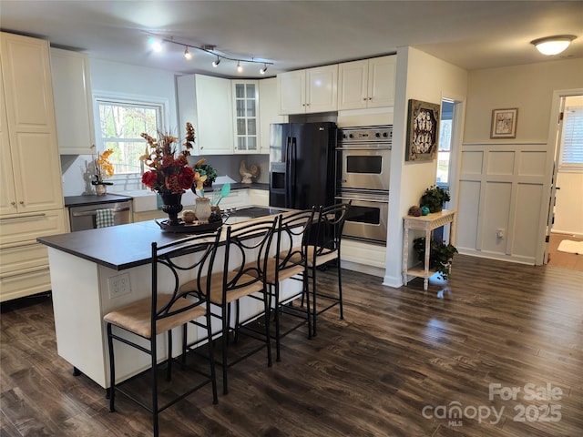 kitchen featuring dark wood finished floors, glass insert cabinets, appliances with stainless steel finishes, white cabinetry, and a kitchen bar