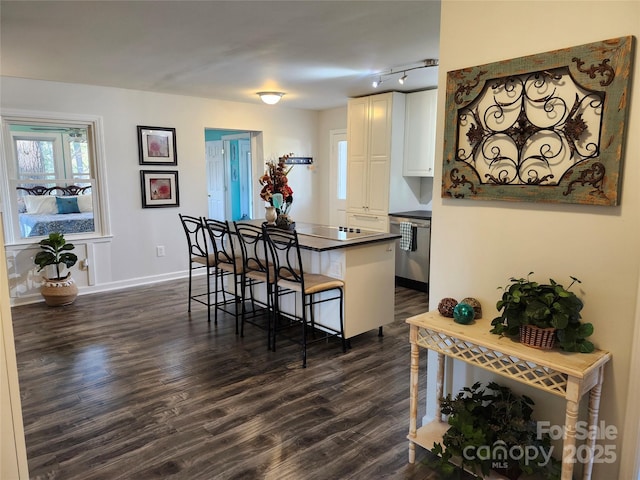 kitchen with dark wood-style flooring, a breakfast bar area, dark countertops, white cabinets, and baseboards