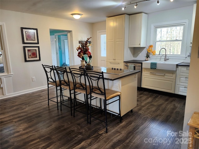 kitchen featuring dark countertops, a kitchen island, a breakfast bar, dark wood-style flooring, and a sink