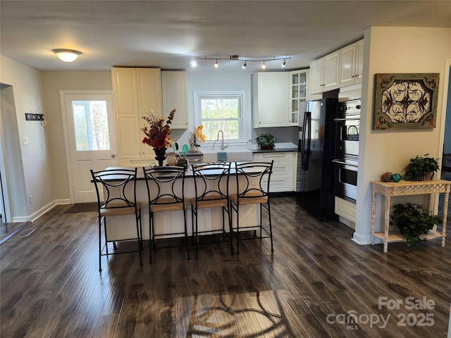 kitchen featuring glass insert cabinets, white cabinetry, black fridge with ice dispenser, and double oven