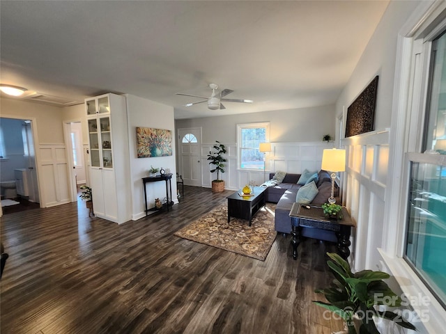 living room with a ceiling fan, a decorative wall, and dark wood-type flooring