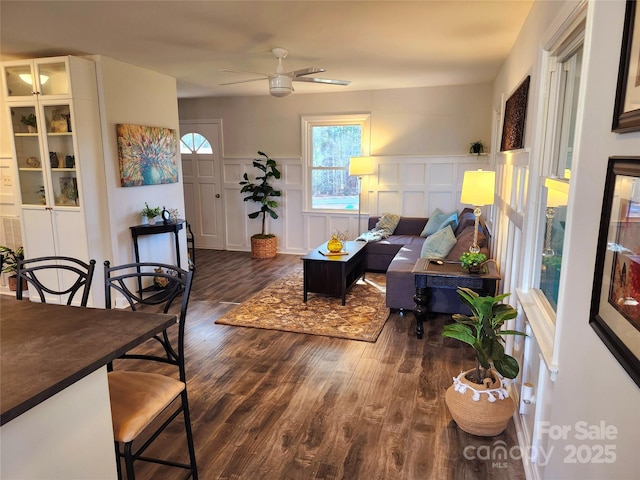 living area with wainscoting, ceiling fan, dark wood finished floors, and a decorative wall