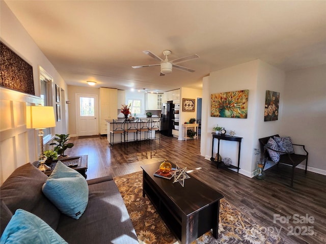 living room featuring dark wood-type flooring, a ceiling fan, and baseboards