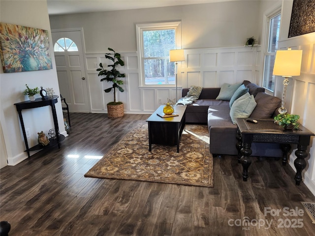 living area featuring dark wood-style flooring, wainscoting, and a decorative wall