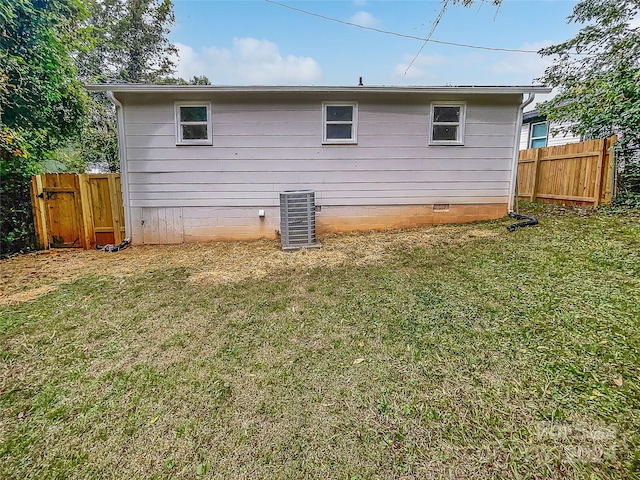 rear view of house with central AC unit and a yard