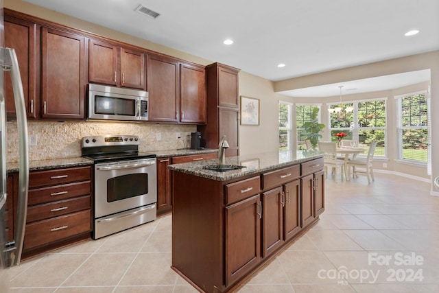 kitchen with stone countertops, a center island with sink, appliances with stainless steel finishes, backsplash, and decorative light fixtures