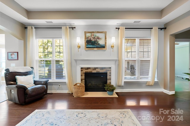 living area featuring plenty of natural light, dark hardwood / wood-style floors, a raised ceiling, and a tile fireplace