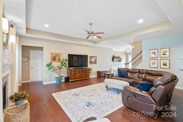 living room with dark wood-type flooring, a tray ceiling, ceiling fan, and a fireplace