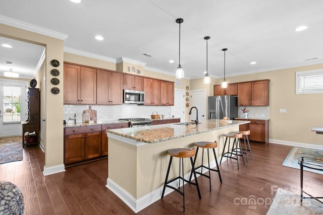 kitchen featuring dark wood-type flooring, a center island with sink, a kitchen breakfast bar, appliances with stainless steel finishes, and decorative light fixtures