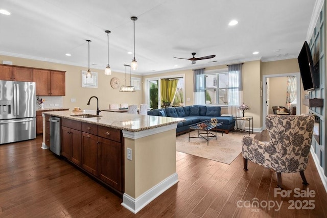 kitchen featuring sink, an island with sink, appliances with stainless steel finishes, decorative light fixtures, and light stone counters