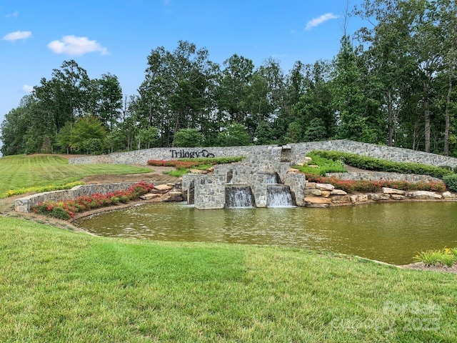 community / neighborhood sign featuring a lawn and a water view