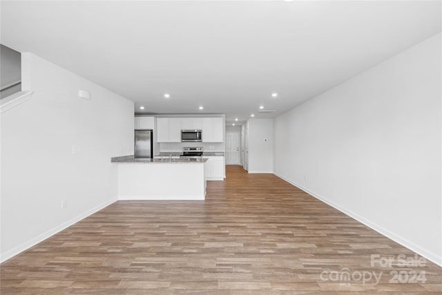 kitchen with light hardwood / wood-style floors, white cabinetry, kitchen peninsula, stainless steel appliances, and light stone countertops