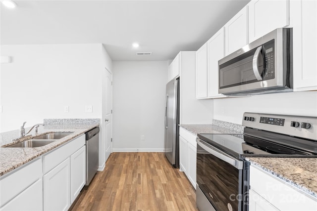 kitchen with appliances with stainless steel finishes, light hardwood / wood-style floors, white cabinetry, light stone counters, and sink