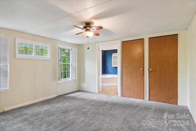 unfurnished bedroom with two closets, light carpet, connected bathroom, and ceiling fan