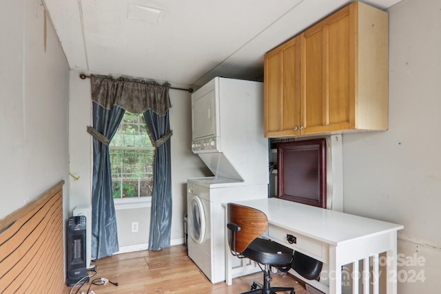 clothes washing area featuring stacked washer / drying machine, light hardwood / wood-style floors, and cabinets