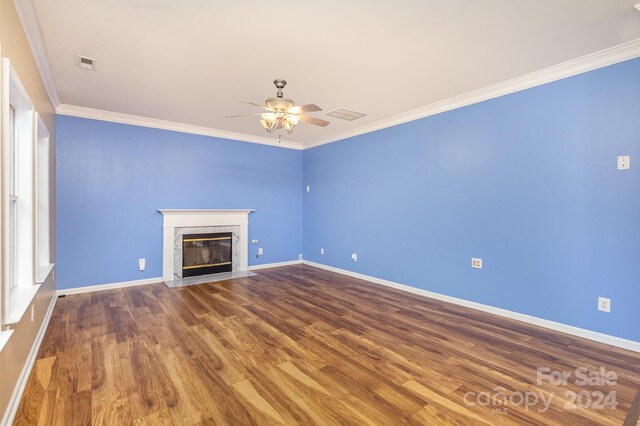 unfurnished living room featuring wood-type flooring, a premium fireplace, ceiling fan, and crown molding